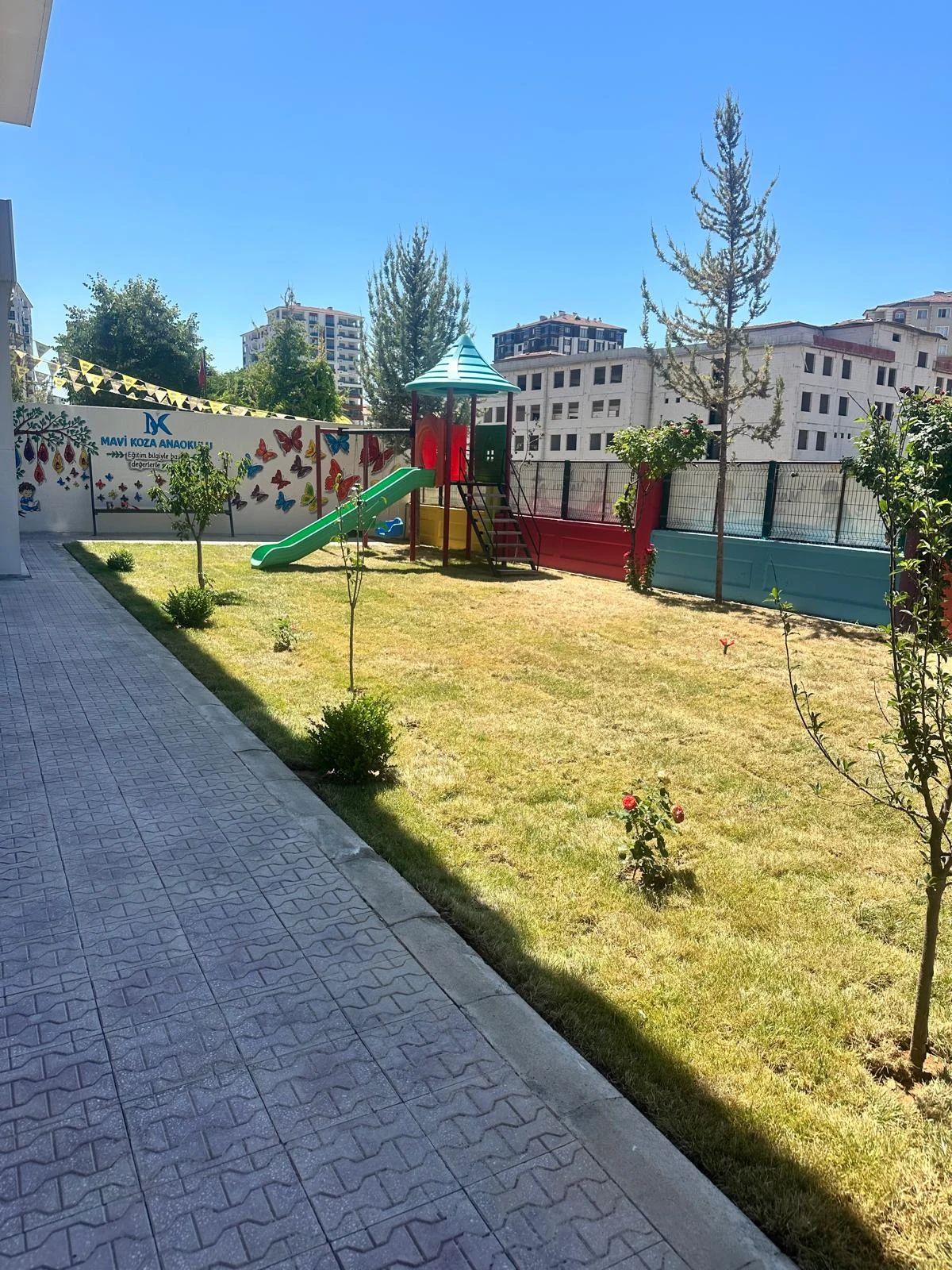 Mavi Koza bahçesinde çim alan, ağaçlar ve oyun grubu